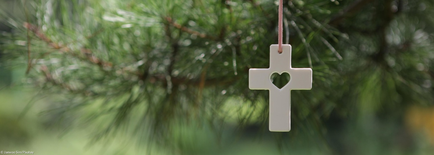 weißes Kreuz mit Herz vor einem Baum