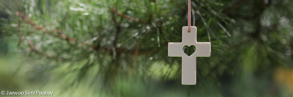 weißes Kreuz mit Herz vor einem Baum